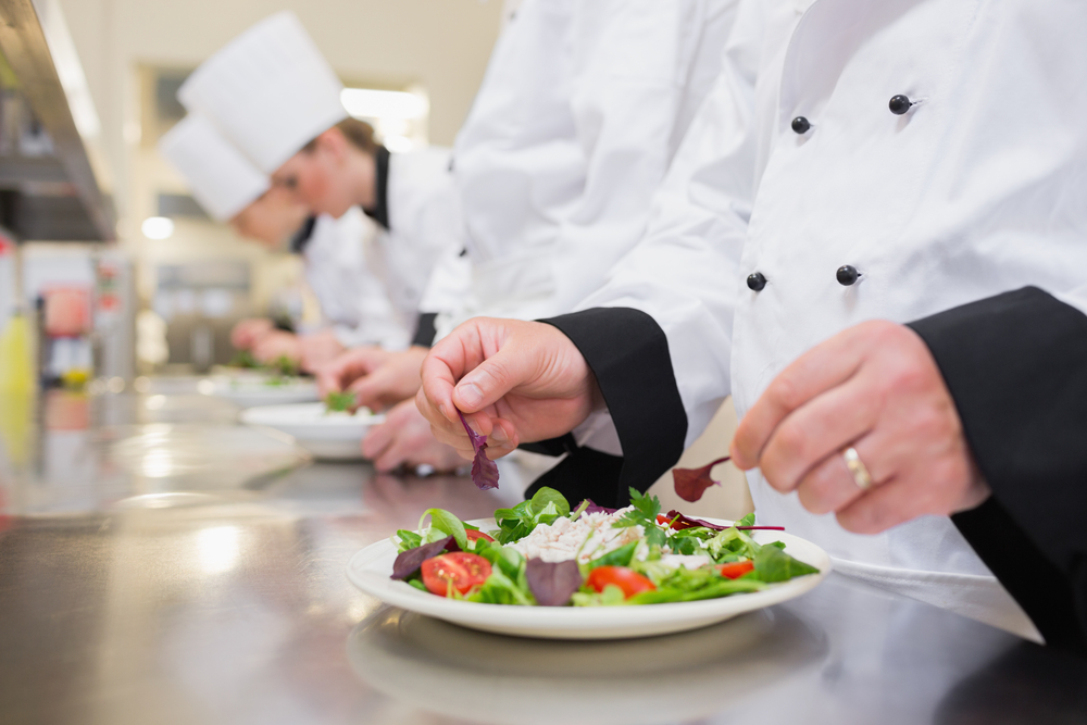 Chef garnishing salads in the kitchen with others garnishing their salads